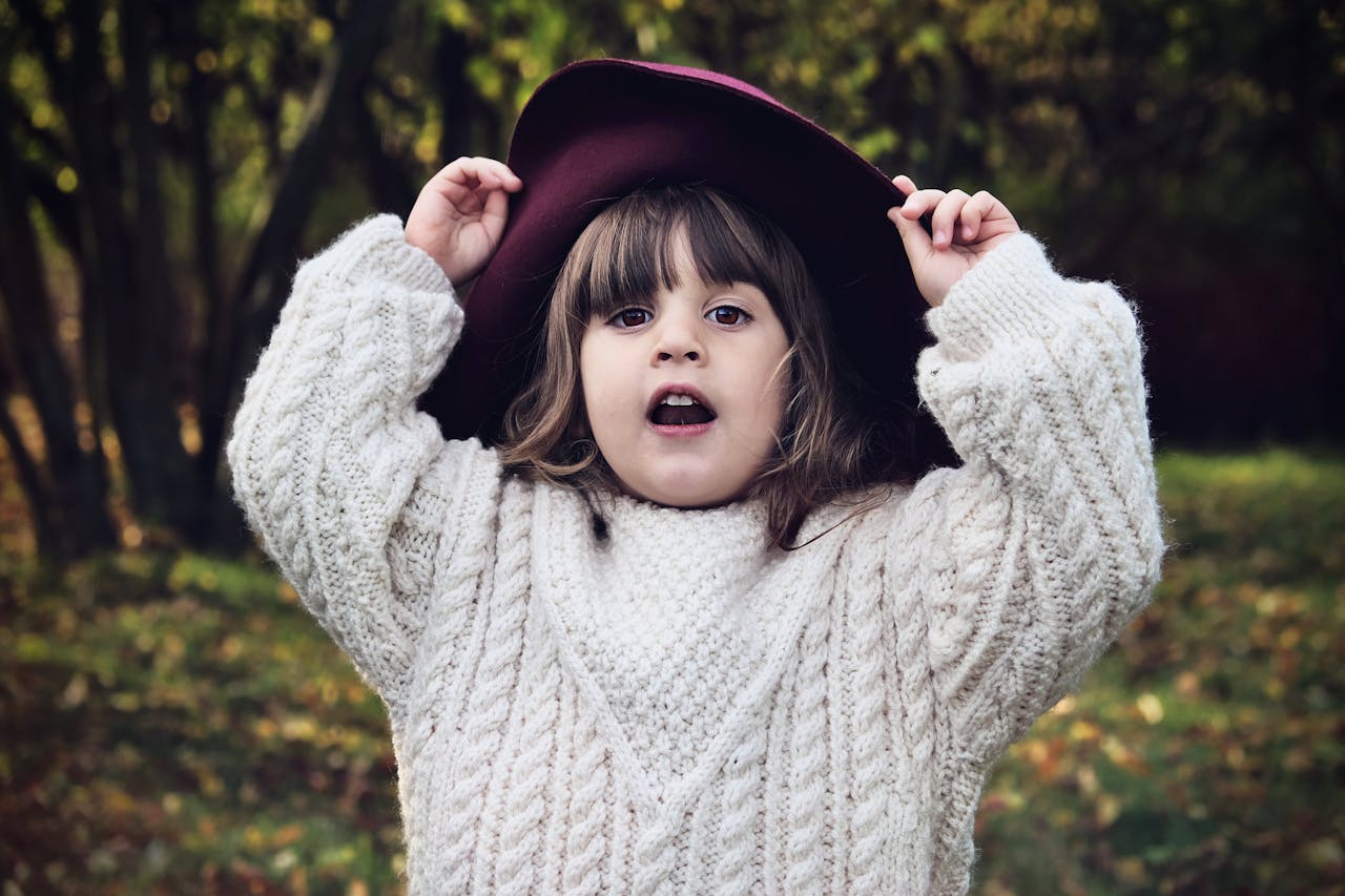 A cute girl in a white sweater and hat posing playfully in a park during fall.