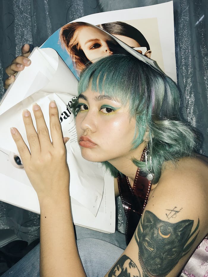 Stylish young woman with colorful hair and tattoos posing with a magazine, exuding a chic modern vibe.